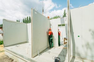 建筑工人在绿色工作服和橙色安全帽指导预制墙面板在建筑施工、混凝土楼板