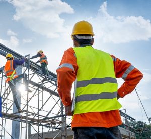 建筑工头绿色安全背心和黄色安全帽看工人爬钢建筑框架
