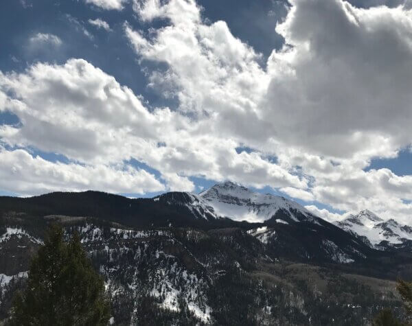 积雪覆盖的山和树下面的照片,白云在蓝色的天空