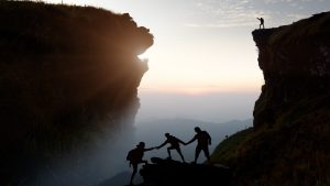 轮廓的人互相帮助爬岩石日落时分,巨大的岩层骨架,信任